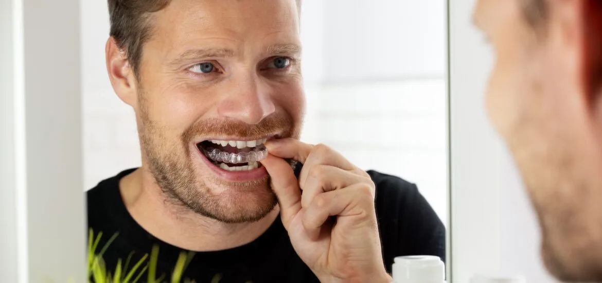 middle aged man looking in the mirror, inserting his Invisalign