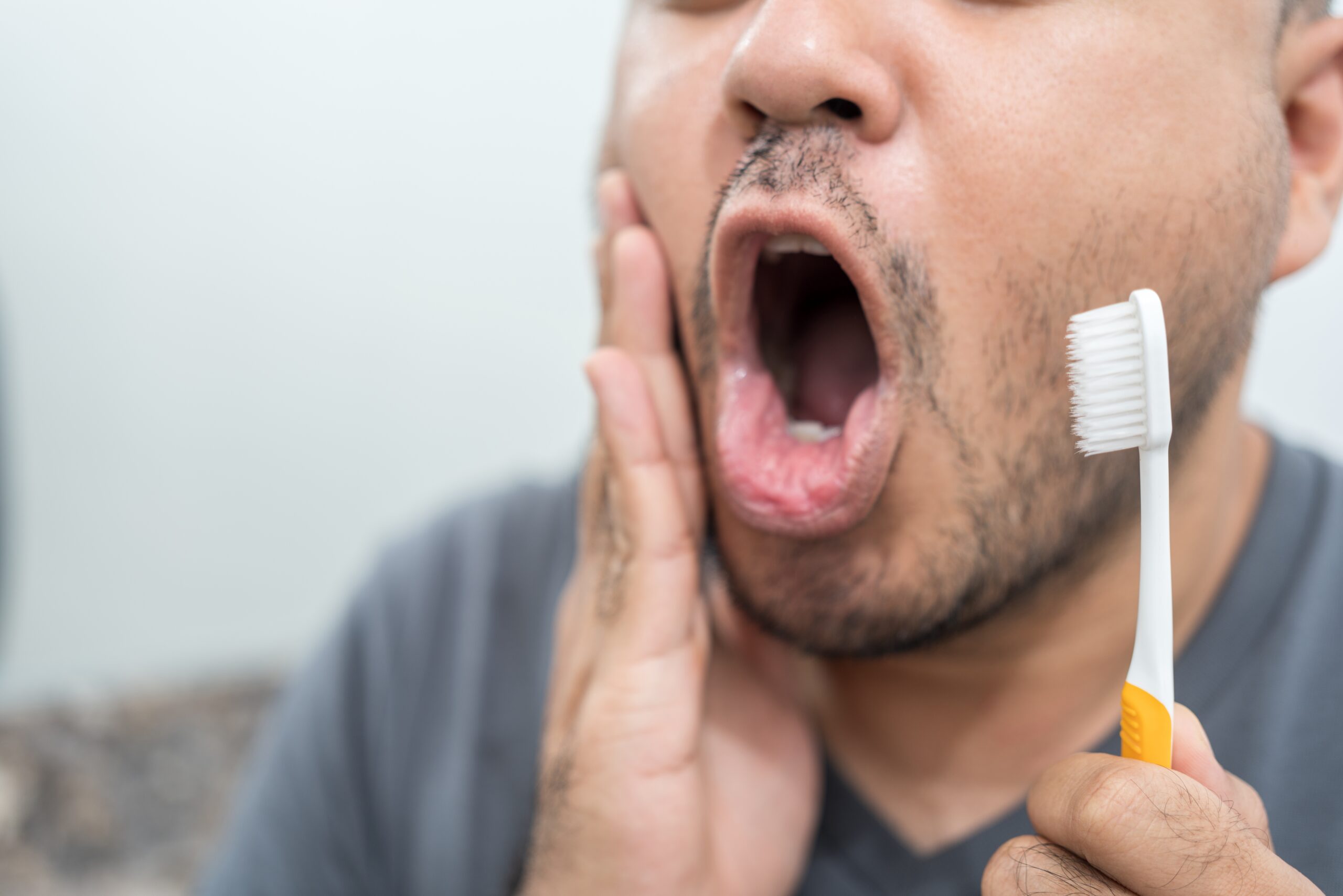 closeup of a man brushing his teeth holding jaw, severe tooth pain